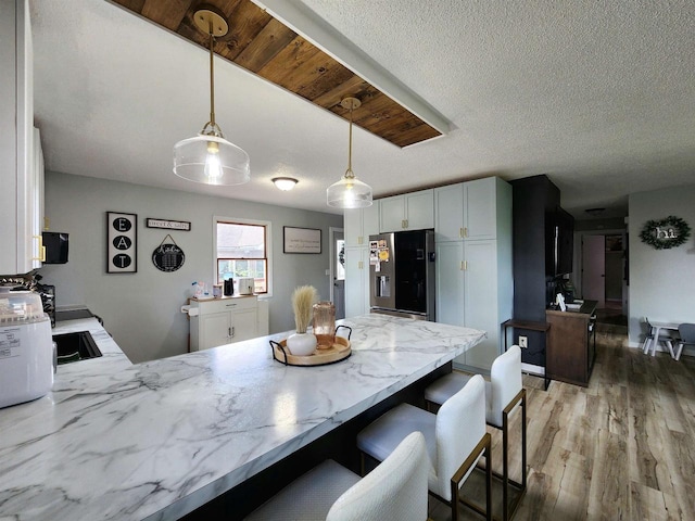307 W Jackson St, Tomah, WI 54660 - kitchen with stainless steel refrigerator with ice dispenser, light stone countertops, light wood-style floors, a peninsula, and decorative light fixtures