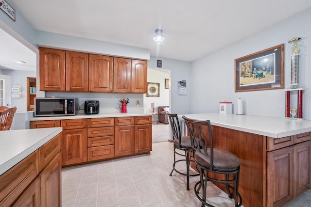 1116 Lake Park Rd, Menasha, WI 54952 - kitchen with stainless steel microwave, a breakfast bar, brown cabinetry, and light countertops