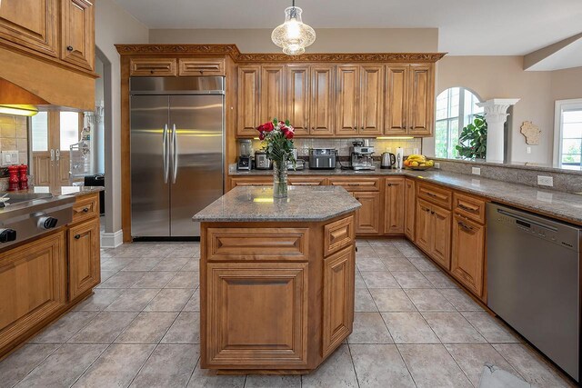 18290 Prairie Falcon Ln, Brookfield, WI 53045 - kitchen with stainless steel appliances, light stone counters, brown cabinetry, a kitchen island, and decorative backsplash