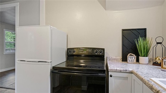 2572 90th St, Eau Claire, WI 54703 - kitchen featuring black range with electric stovetop, freestanding refrigerator, white cabinetry, and wood finished floors