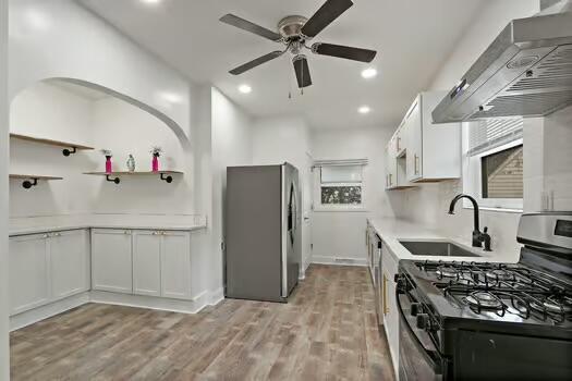 1107 Perry Ave, Racine, WI 53406 - kitchen with appliances with stainless steel finishes, a sink, wall chimney exhaust hood, a ceiling fan, and light wood finished floors