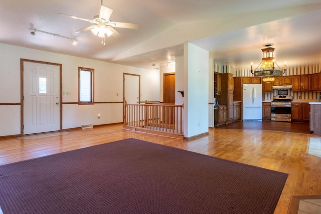 W5670 School Rd, Walworth, WI 53184 - unfurnished living room featuring light wood-type flooring, vaulted ceiling, a ceiling fan, a chandelier, and baseboards