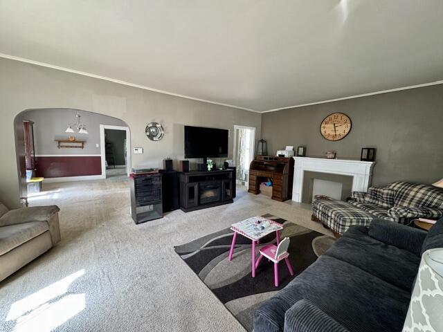 219 E 9th St, Fond Du Lac, WI 54935 - living room featuring arched walkways, light carpet, crown molding, a fireplace, and baseboards