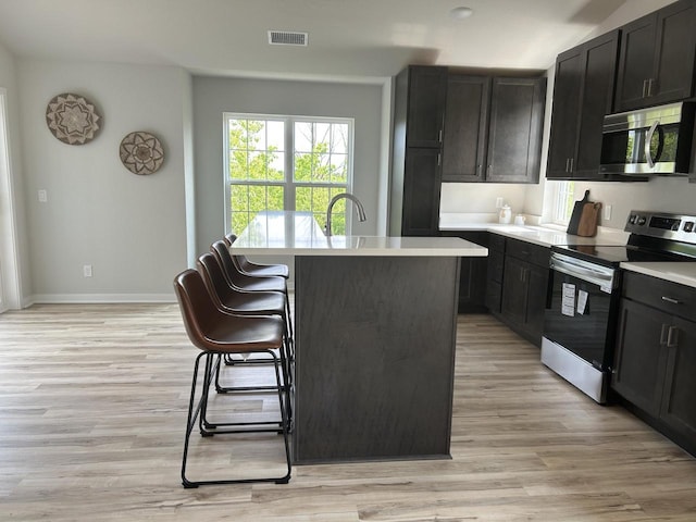 W141N9978 Seven Pines Way Unit 204, Germantown, WI 53022 - kitchen with appliances with stainless steel finishes, a kitchen island, light wood-type flooring, and a kitchen bar