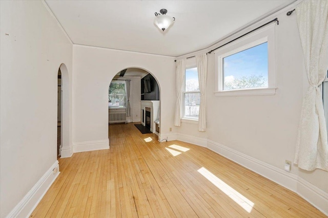 2127 Tower Ave, Superior, WI 54880 - unfurnished living room featuring radiator, arched walkways, a fireplace, wood-type flooring, and baseboards