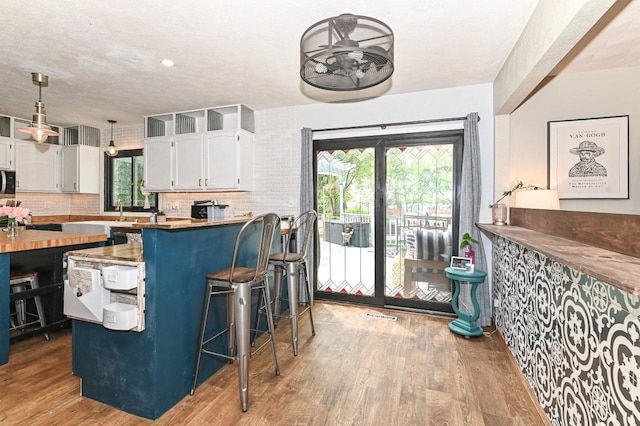 1081 E Elm Rd, Oak Creek, WI 53154 - kitchen with white cabinetry, wood finished floors, plenty of natural light, a breakfast bar area, and a textured ceiling