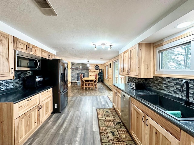 N11893 Pratt Rd, Elcho, WI 54428 - kitchen featuring stainless steel appliances, dark countertops, a sink, light brown cabinetry, and a stone fireplace