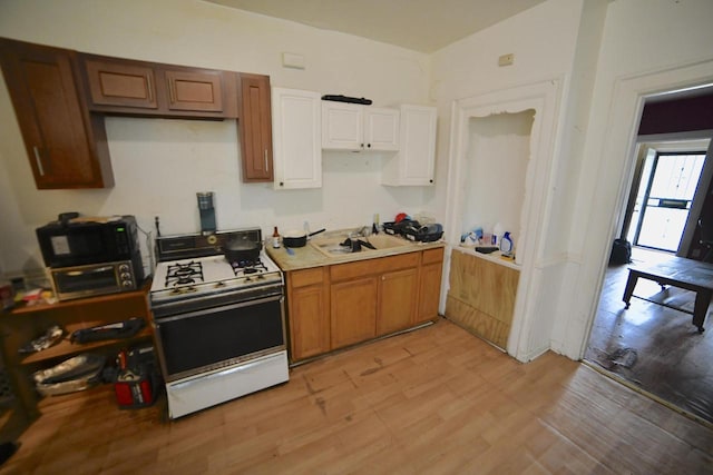1925 W Center St, Milwaukee, WI 53206 - kitchen featuring white gas range, a sink, light wood-style floors, light countertops, and white cabinets