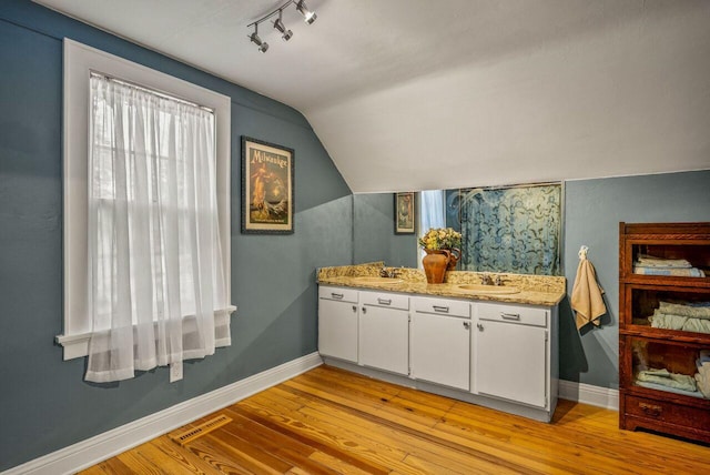 5642 N Argyle Ave, Glendale, WI 53209 - bathroom featuring baseboards, wood finished floors, rail lighting, vaulted ceiling, and double vanity