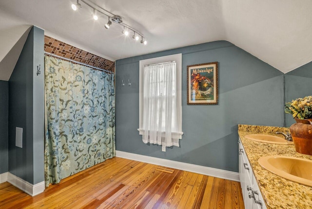 5642 N Argyle Ave, Glendale, WI 53209 - full bath with wood finished floors, baseboards, double vanity, vaulted ceiling, and curtained shower
