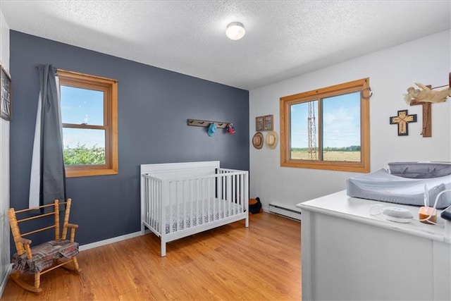 E7065 E County Road B, Colfax, WI 54730 - bedroom featuring a baseboard heating unit, a textured ceiling, light wood-type flooring, and baseboards
