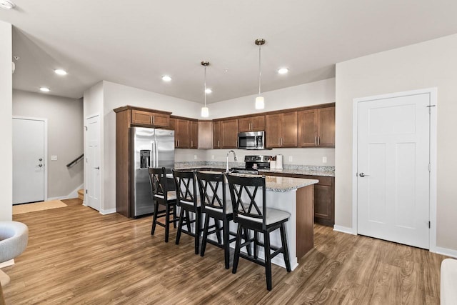 4857 Suelo Rd, Fitchburg, WI 53711 - kitchen featuring stainless steel appliances, light wood-style floors, a center island with sink, decorative light fixtures, and a breakfast bar