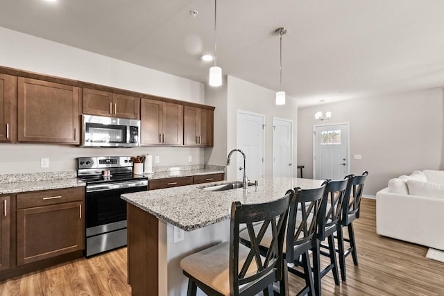 4857 Suelo Rd, Fitchburg, WI 53711 - kitchen featuring appliances with stainless steel finishes, a sink, light wood-style floors, an island with sink, and a chandelier