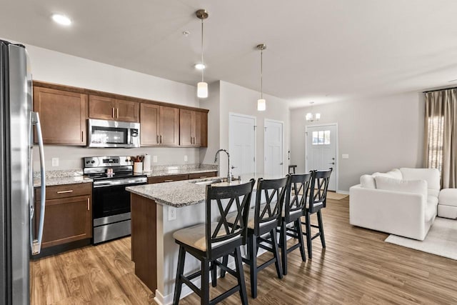4857 Suelo Rd, Fitchburg, WI 53711 - kitchen featuring appliances with stainless steel finishes, a sink, light wood-style floors, open floor plan, and a kitchen breakfast bar