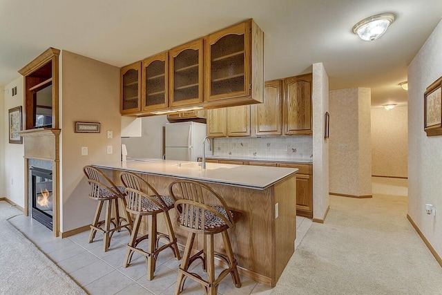 211 Oconomowoc Pkwy, Oconomowoc, WI 53066 - kitchen featuring freestanding refrigerator, a breakfast bar area, glass insert cabinets, a peninsula, and baseboards