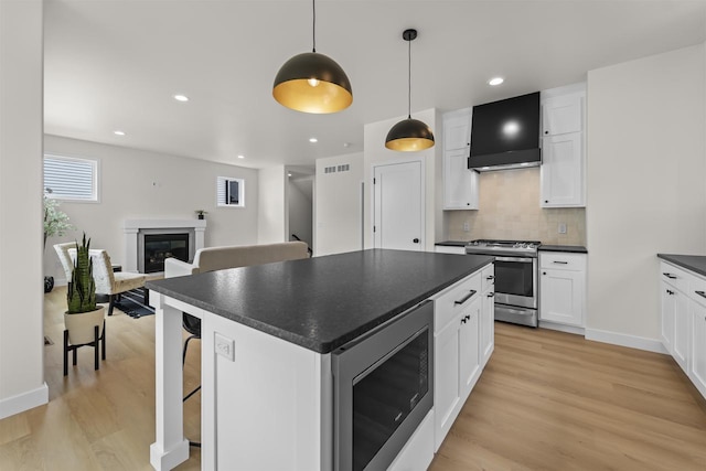 727 Schubert St, Verona, WI 53593 - kitchen featuring appliances with stainless steel finishes, wall chimney range hood, dark countertops, light wood-style floors, and a glass covered fireplace