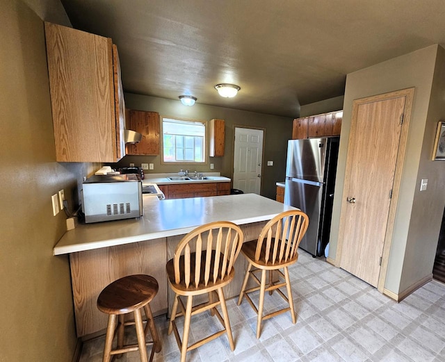 1114 W St, Racine, WI 53404 - kitchen featuring freestanding refrigerator, wall chimney range hood, a sink, a peninsula, and light flooring