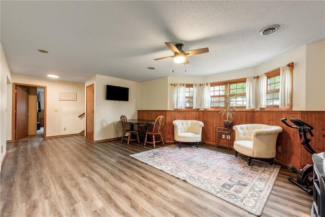4868 183rd St, Chippewa Falls, WI 54729 - living area featuring a ceiling fan, light wood-type flooring, wood walls, a wainscoted wall, and a textured ceiling