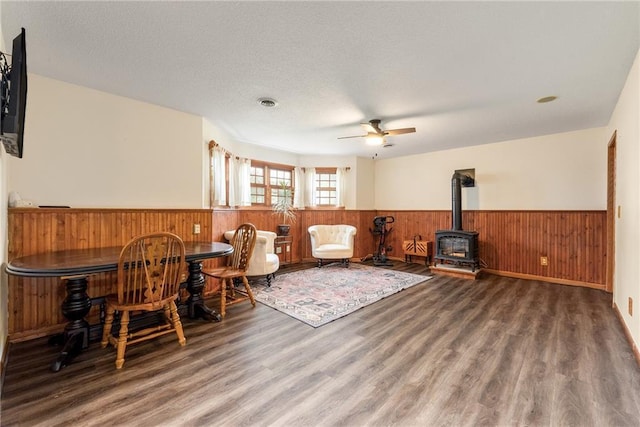 4868 183rd St, Chippewa Falls, WI 54729 - living area with a wainscoted wall, wooden walls, a wood stove, ceiling fan, and wood finished floors
