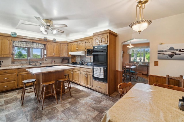 W7211 Pine Rd, Thorp, WI 54771 - kitchen with a sink, arched walkways, light countertops, brown cabinetry, and a wainscoted wall