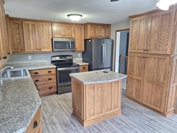 810 Railroad Ave, Viroqua, WI 54665 - kitchen with stainless steel appliances, a sink, light wood finished floors, a textured ceiling, and a kitchen island