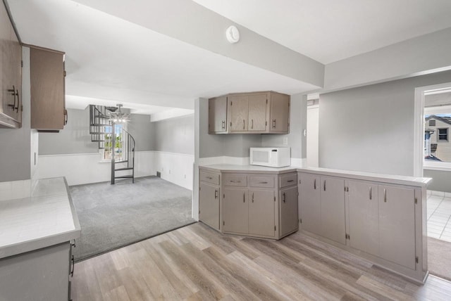 1925 Salisbury Rd, West Bend, WI 53090 - kitchen with white microwave, wainscoting, a chandelier, light wood finished floors, and light countertops
