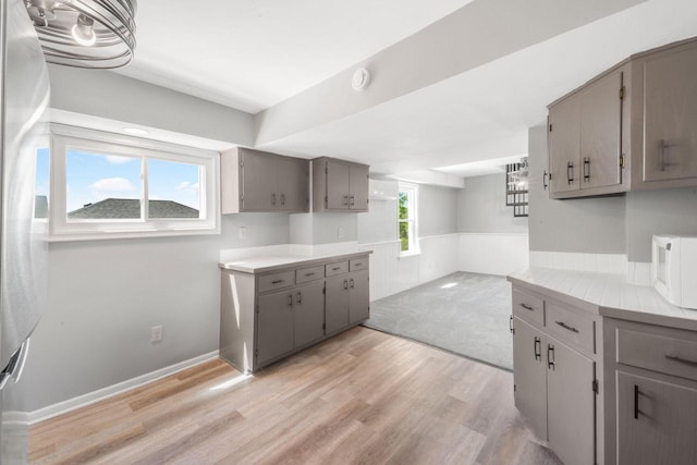 1925 Salisbury Rd, West Bend, WI 53090 - kitchen featuring gray cabinetry, white microwave, light wood-style floors, light countertops, and a wainscoted wall