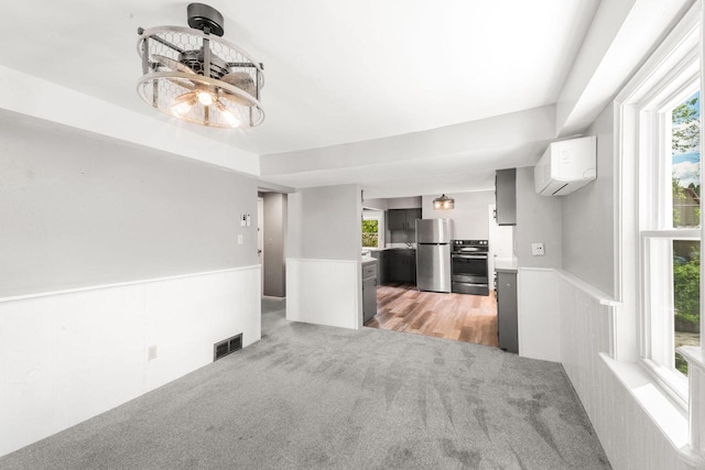 1925 Salisbury Rd, West Bend, WI 53090 - unfurnished living room featuring wainscoting, a wall mounted air conditioner, light carpet, and plenty of natural light