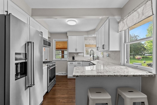 751 Warsaw St, Menasha, WI 54952 - kitchen featuring high end appliances, a peninsula, light stone countertops, and white cabinetry