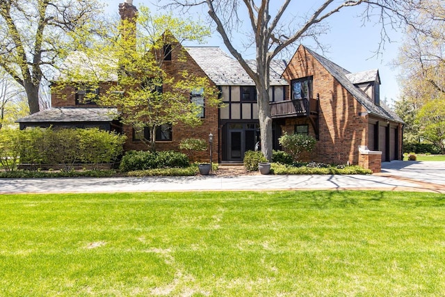 1030 Washington Ave, Oshkosh, WI 54901 - tudor-style house featuring a balcony, a front lawn, concrete driveway, brick siding, and a garage