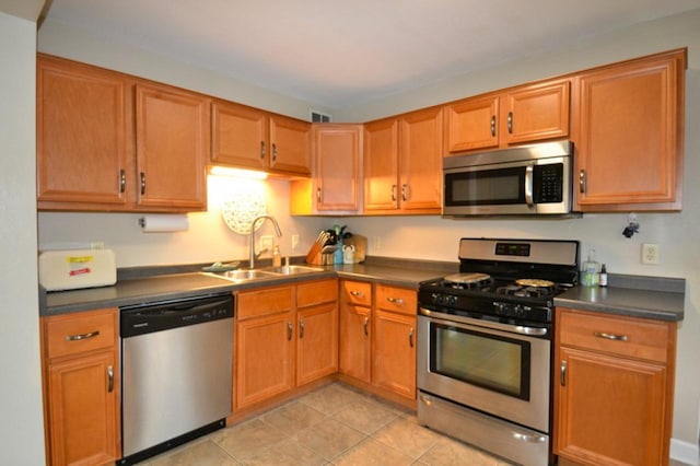 10432 W Manor Park Dr, West Allis, WI 53227 - kitchen with stainless steel appliances, a sink, dark countertops, light tile patterned flooring, and brown cabinetry
