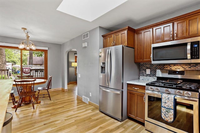 4705 Winnequah Rd, Monona, WI 53716 - kitchen with appliances with stainless steel finishes, arched walkways, light wood finished floors, a chandelier, and tasteful backsplash