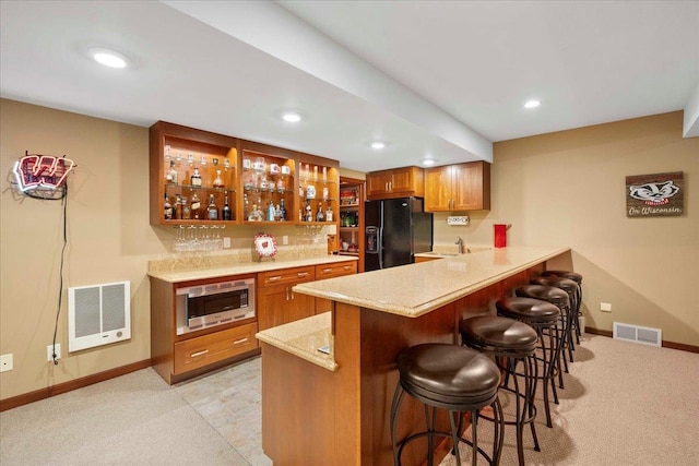 7197 Welford Pl, Sun Prairie, WI 53590 - kitchen with black fridge with ice dispenser, stainless steel microwave, heating unit, a breakfast bar, and baseboards
