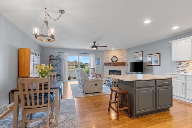 1243 Pond View Cir, De Pere, WI 54115 - kitchen with white cabinetry, gray cabinets, ceiling fan, a stone fireplace, and light wood-style flooring