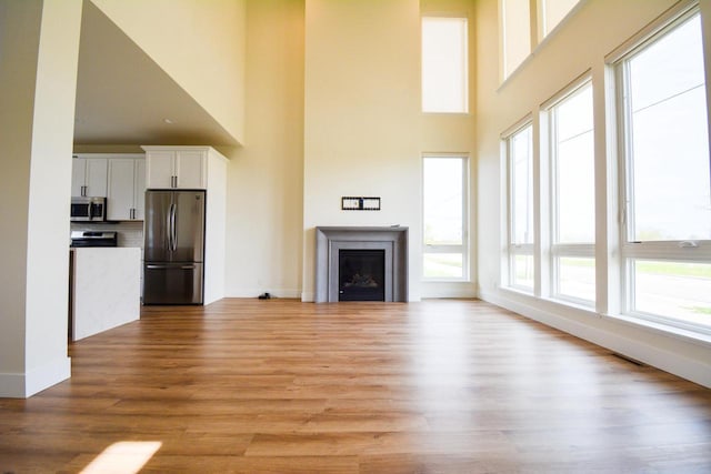 4200 E Lake Vista Blvd, Oak Creek, WI 53154 - unfurnished living room featuring a towering ceiling, light wood finished floors, baseboards, and a fireplace