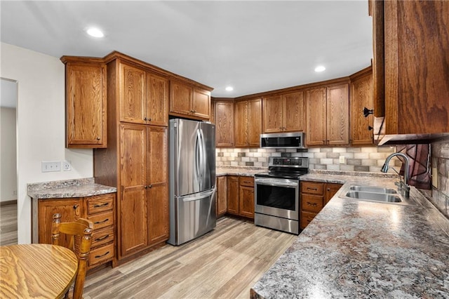 12924 Thomas St, Osseo, WI 54758 - kitchen with appliances with stainless steel finishes, a sink, brown cabinets, light wood finished floors, and decorative backsplash