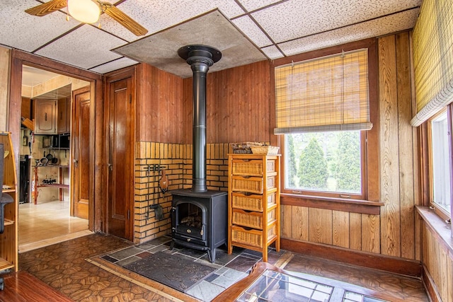 917 Whitewater Ave, Fort Atkinson, WI 53538 - detailed view of a wood stove, wood walls, a ceiling fan, a drop ceiling, and baseboards