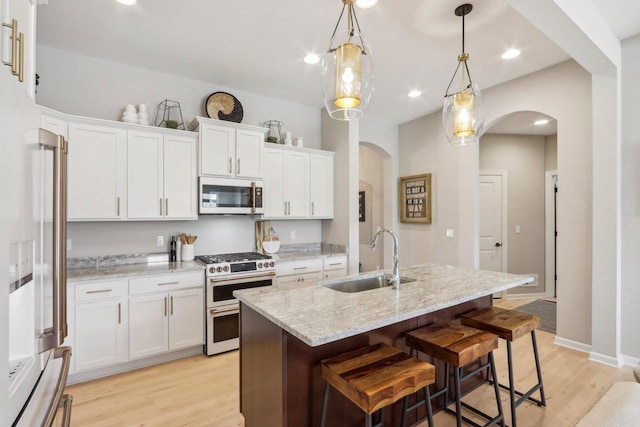 1766 Derby Ln, Oconomowoc, WI 53066 - kitchen featuring stainless steel appliances, arched walkways, a sink, light wood-type flooring, and white cabinetry