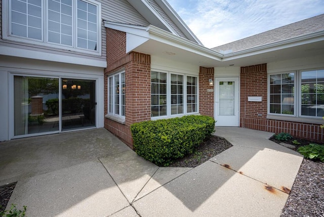 8707 Westlake Dr, Greendale, WI 53129 - view of exterior entry with brick siding, a patio area, and a shingled roof