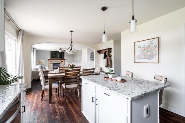 6544 Biscayne Ave, Mount Pleasant, WI 53406 - kitchen featuring arched walkways, a stone fireplace, dark wood-style floors, a center island, and hanging light fixtures