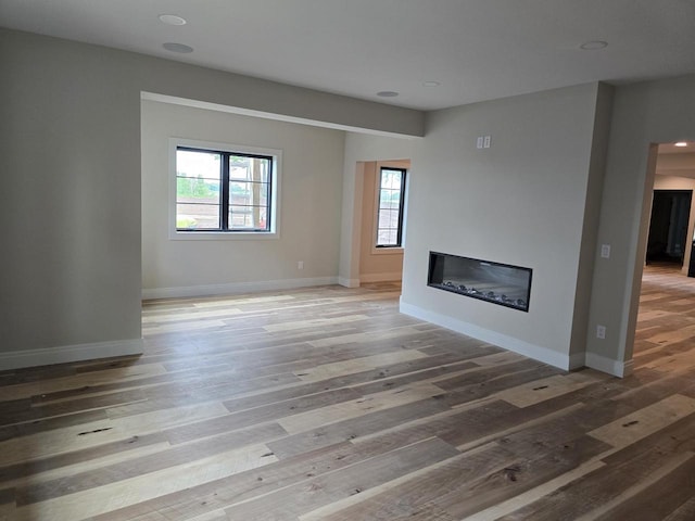 1102 Moll Dr, Waunakee, WI 53597 - unfurnished living room featuring healthy amount of natural light, a glass covered fireplace, light wood-type flooring, baseboards, and recessed lighting