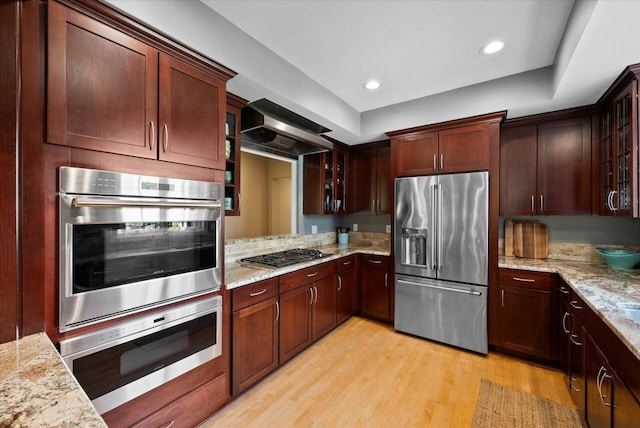 4320 High, Point Beach Lane, Port Washington, WI 53074 - kitchen featuring appliances with stainless steel finishes, wall chimney exhaust hood, light wood-style floors, glass insert cabinets, and light stone counters
