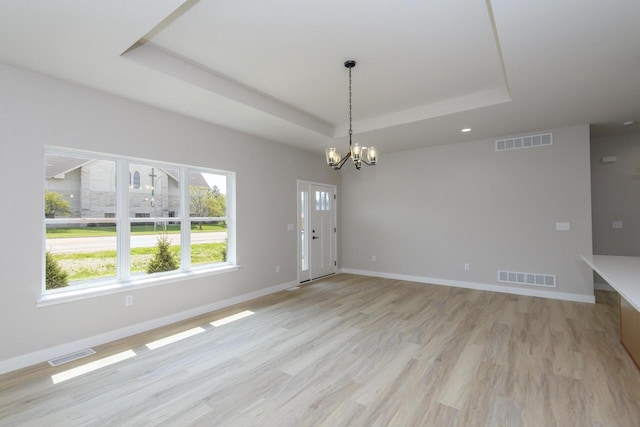 20840 Gray St, Lannon, WI 53046 - unfurnished dining area featuring a tray ceiling, a chandelier, light wood finished floors, and baseboards
