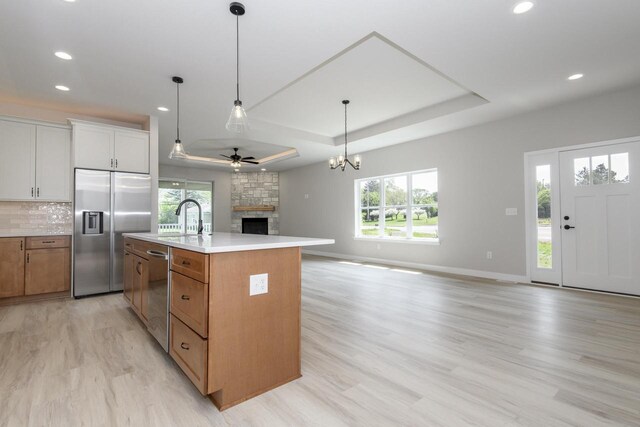 20840 Gray St, Lannon, WI 53046 - kitchen featuring stainless steel appliances, a tray ceiling, a stone fireplace, a ceiling fan, and open floor plan