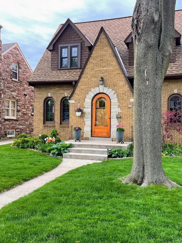620 W Rock Pl, Glendale, WI 53209 - tudor house featuring a shingled roof, a front lawn, and brick siding