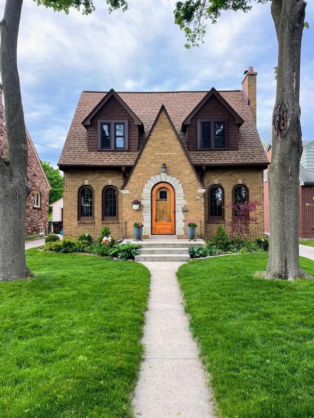 620 W Rock Pl, Glendale, WI 53209 - tudor-style house with roof with shingles, a chimney, and a front yard