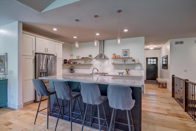 5508 Midmoor Rd, Monona, WI 53716 - kitchen with open shelves, wall chimney range hood, stainless steel refrigerator with ice dispenser, light wood finished floors, and light stone countertops