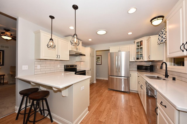 504 Sand Dr, West Bend, WI 53095 - kitchen featuring appliances with stainless steel finishes, under cabinet range hood, a peninsula, tasteful backsplash, and recessed lighting