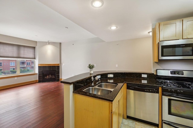 333 W Mifflin St Unit 8100, Madison, WI 53703 - kitchen featuring appliances with stainless steel finishes, a sink, a peninsula, a tiled fireplace, and dark stone counters