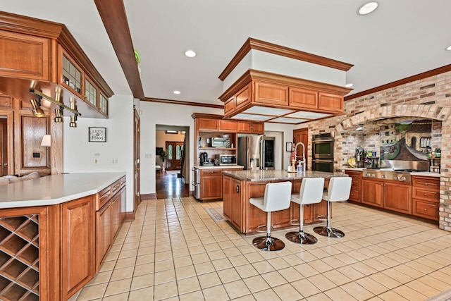 S82W15980 Bass Bay Ln, Muskego, WI 53150 - kitchen featuring stainless steel appliances, light tile patterned floors, brown cabinets, a breakfast bar, and crown molding